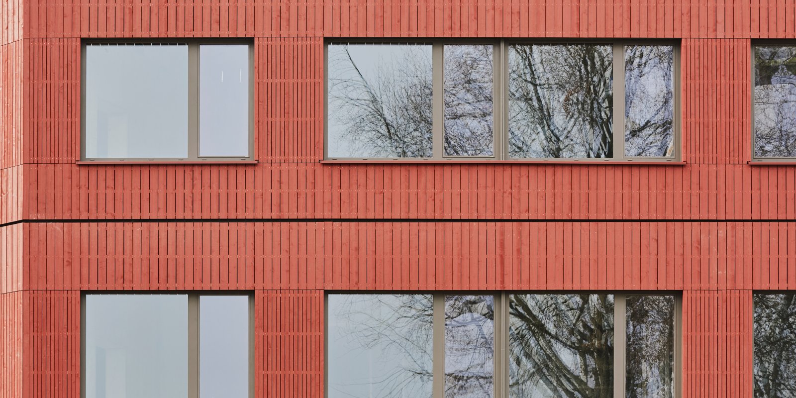 Detailansicht der roten Holzfassade mit vertikaler Schalung und Fensterbändern an der Grundschule Freiberg
