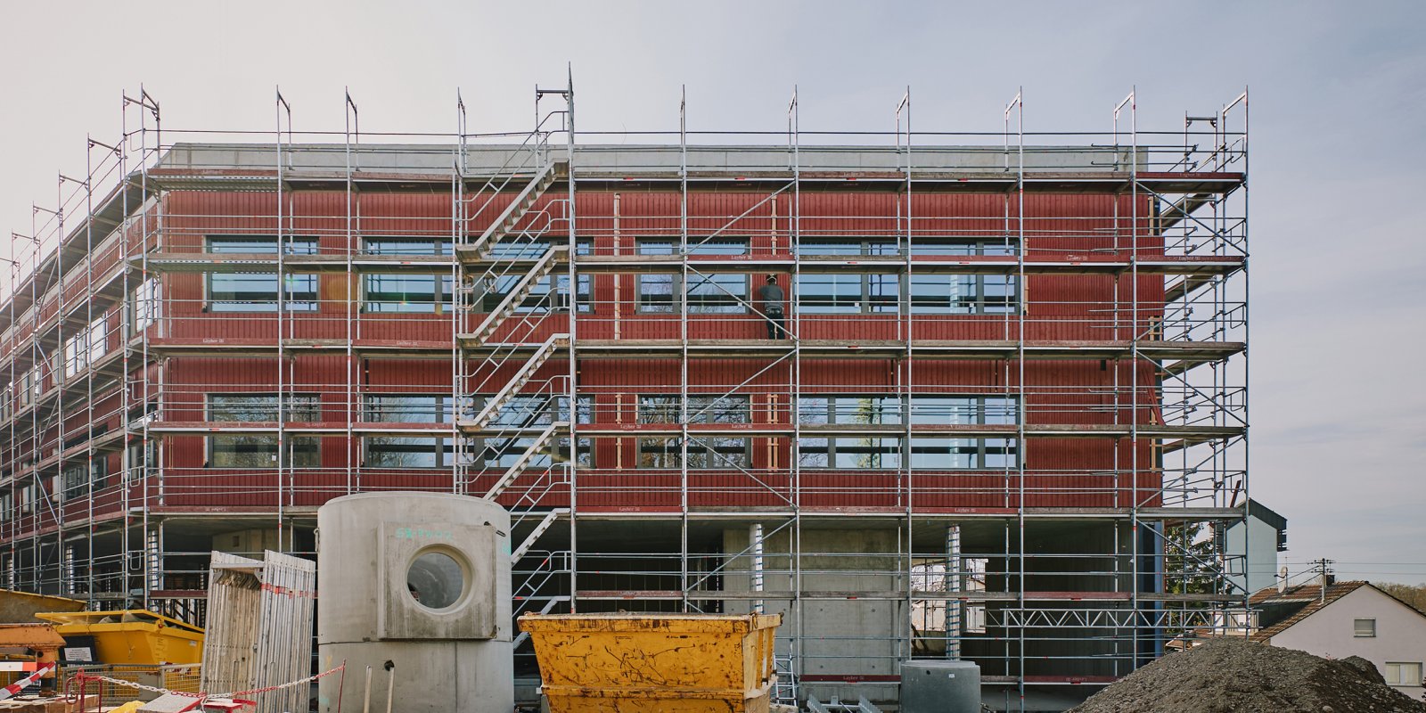 Baustelle der Grundschule Freiberg mit Gerüst, roter Holzfassade und Betontragwerk während der Montagephase