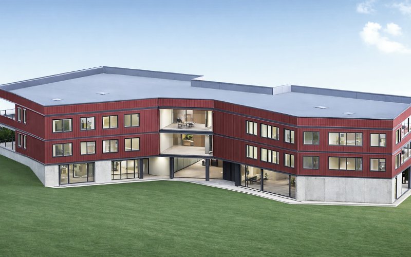Visualisierung moderne Grundschule in Freiberg mit roter Holzfassade, Beton-Skelettbau und klar gegliederter Architektur in nachhaltiger Hybridbauweise