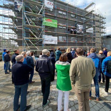 EIne Gruppe von Menschen steht vor dem im Bau befindlichen Laborgebäude der TH Rosenheim, während der Richtspruch gelesen wird