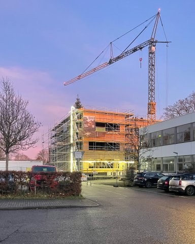 Schulzentrum Bönnigheim in Holzbauweise bei Dämmerung mit Baukran und beleuchtetem Gerüst während der Bauarbeiten.