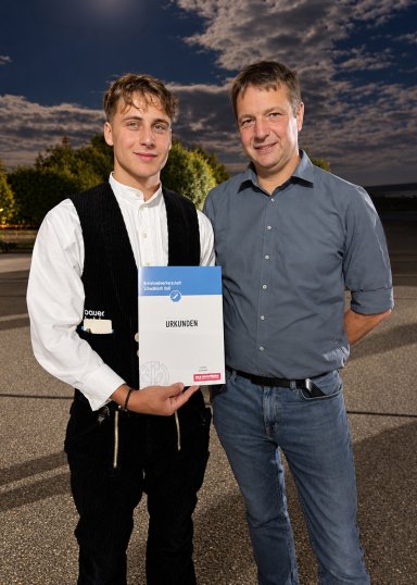 Lucius Schwarz von Bauer Holzbau mit seiner Urkunde neben Meister Heiko Kämmlein bei der Gesellenfreisprechungsfeier 2026.