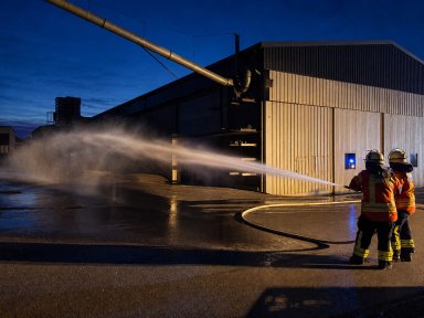 Zwei Feuerwehrleute üben mit einem Löschschlauch die Brandbekämpfung an einer Fertigungshalle von Bauer Holzbau.