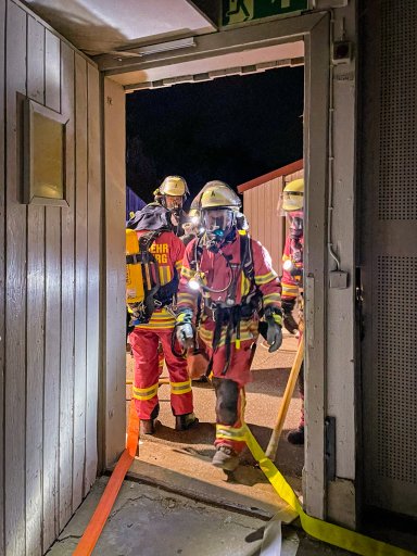 Mehrere Feuerwehrleute mit Atemschutz betreten während der gemeinsamen Übung eine Fertigungshalle von Bauer Holzbau.