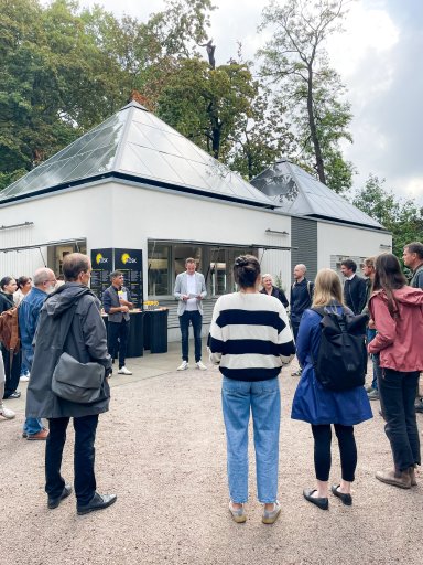 Gäste und Projektbeteiligte versammeln sich vor dem neuen Kiosk KÖSK im Unteren Schlossgarten Stuttgart zur offiziellen Eröffnung mit Ansprache.