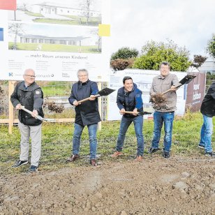 Sieben Projektbeteiligte, darunter Bürgermeister Tobias Strauß, Vertreter des Landkreises, der Kirchengemeinde und des Bauprojekts, stehen beim symbolischen Spatenstich für die neue Kindertagesstätte in Schnelldorf mit Schaufeln auf dem Baugrundstück. Im Hintergrund sind die Bautafel und ein Banner von Bauer Holzbau zu sehen.